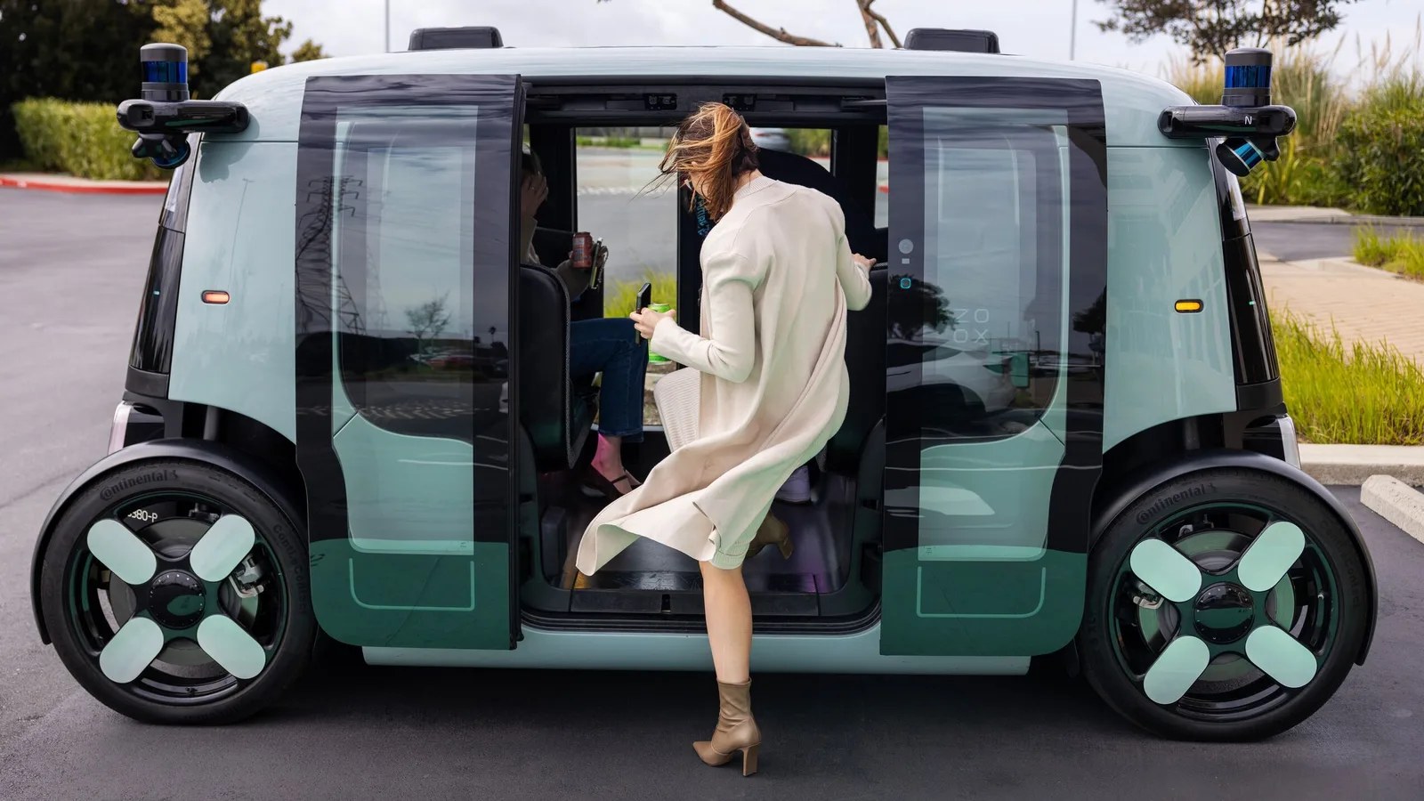 A passenger boarding a Zoox robotaxi, which has no steering wheel and seats four facing each other