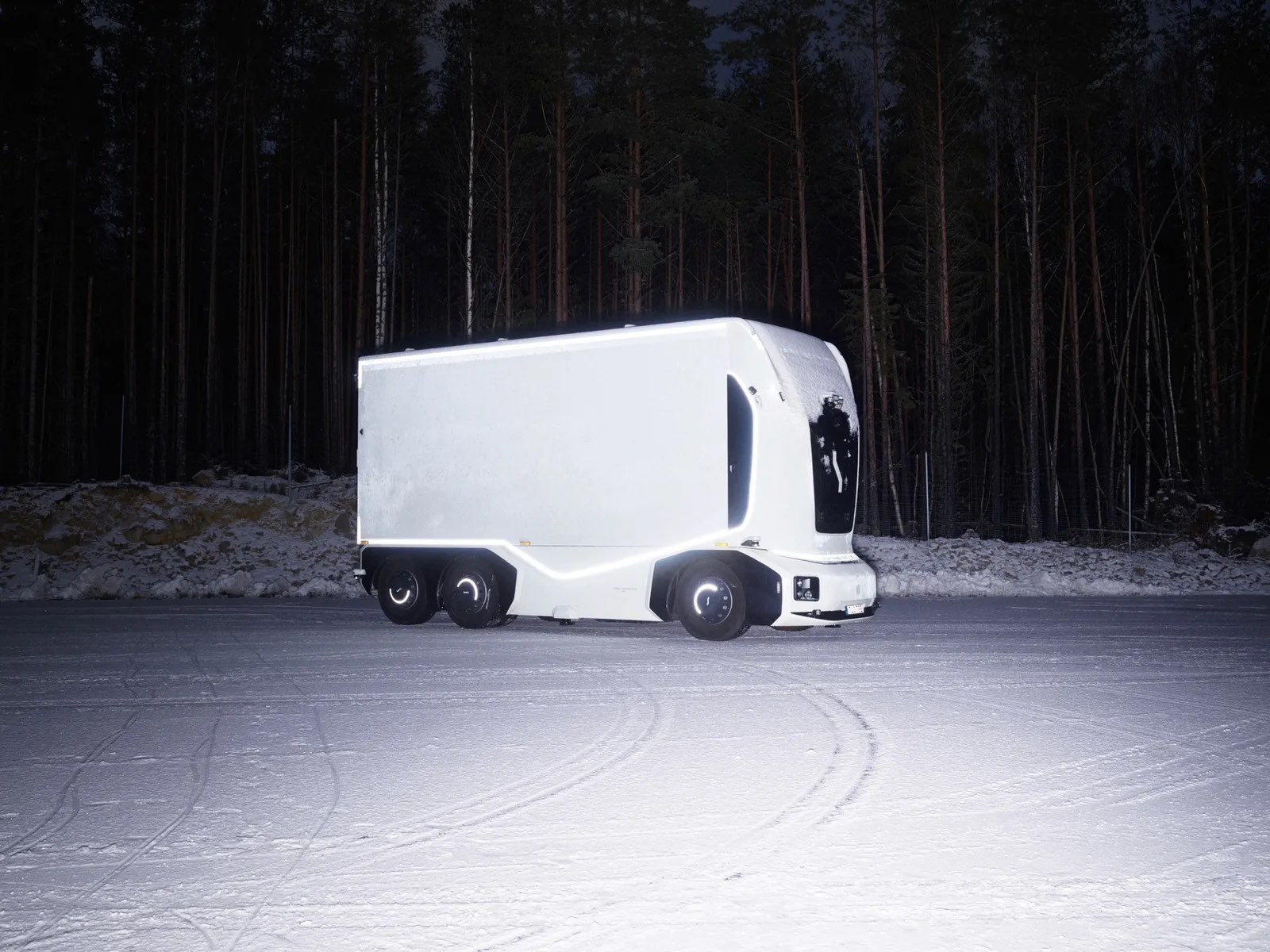 Einride’s cab-less autonomous electric truck, lit from within, parked on snow at night